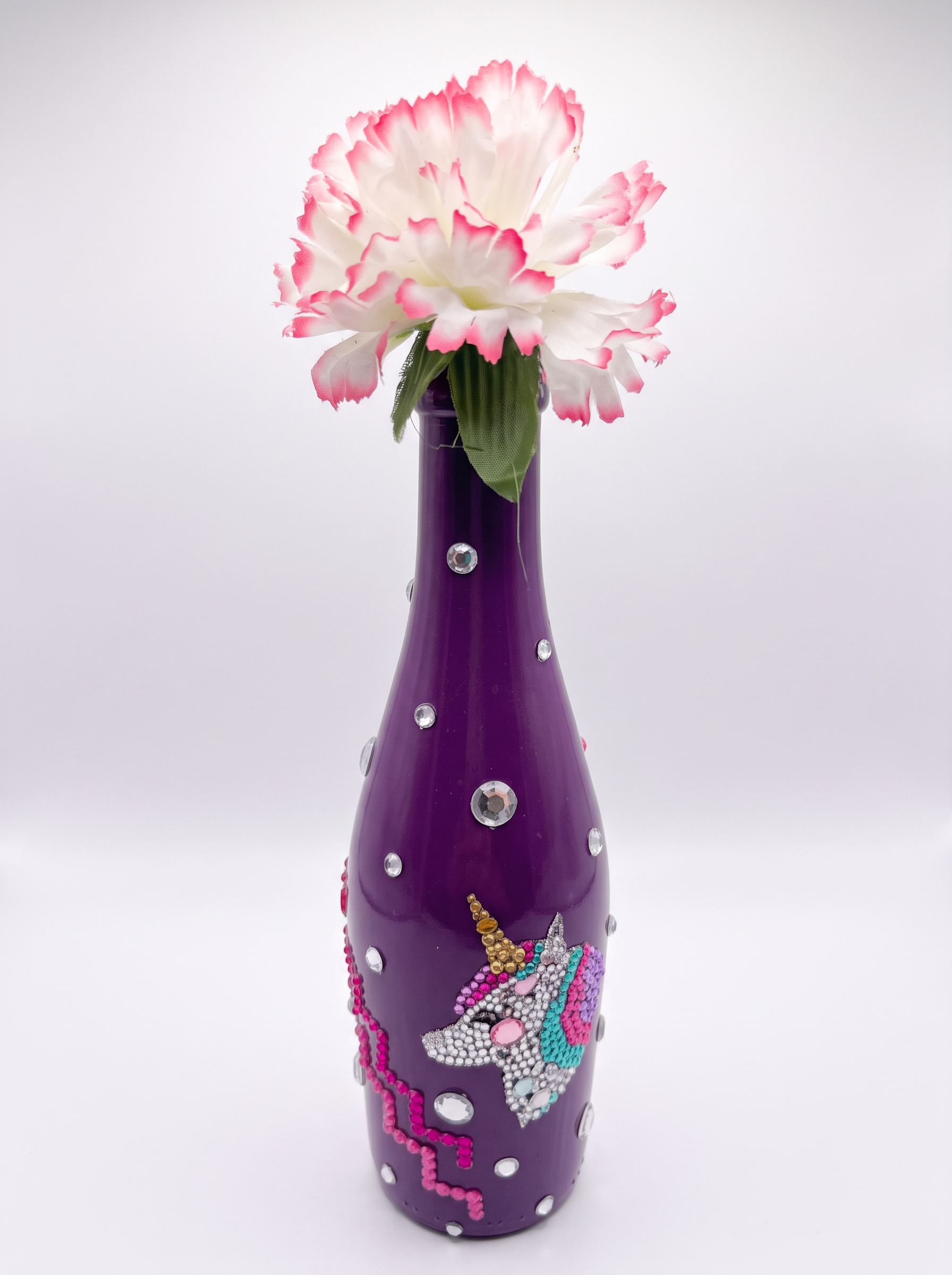 Purple bottle vase with rhinestones, a jeweled unicorn and a white and pink carnation