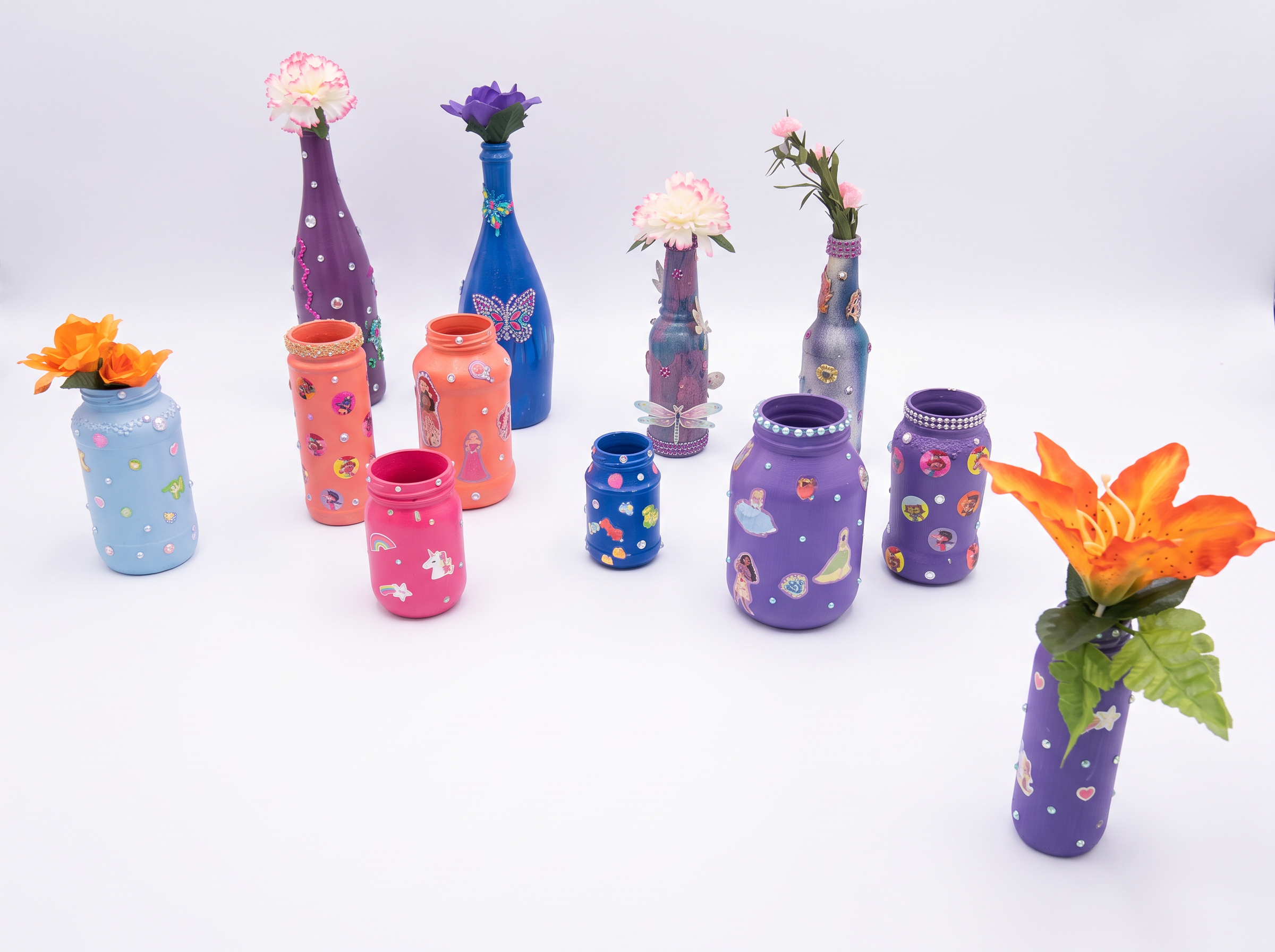 Colorful collection of painted bottle and jar vases with flowers, stickers and rhinestones